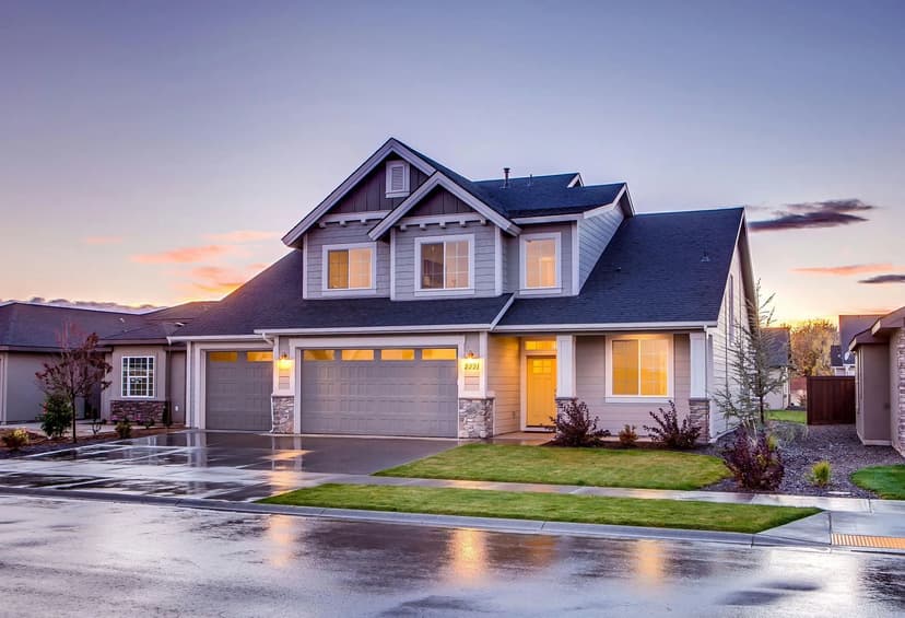 Modern two-story house with garage, lush lawn, and sunset reflections on wet pavement.